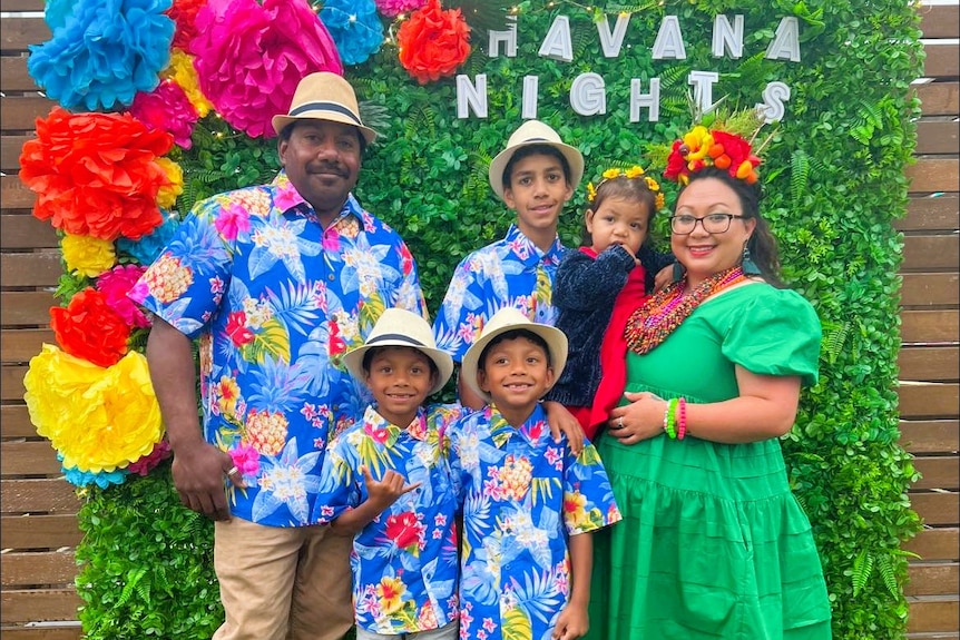 A family of two adults and four children in tropical attire in front of a colourful backdrop that says Havana Nights.