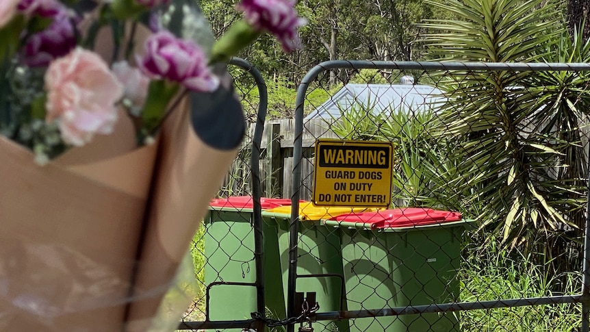 a bunch of flowers tied to a gate, which has a sign warning guard dogs on duty do not enter