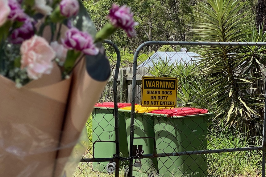a bunch of flowers tied to a gate, which has a sign warning guard dogs on duty do not enter