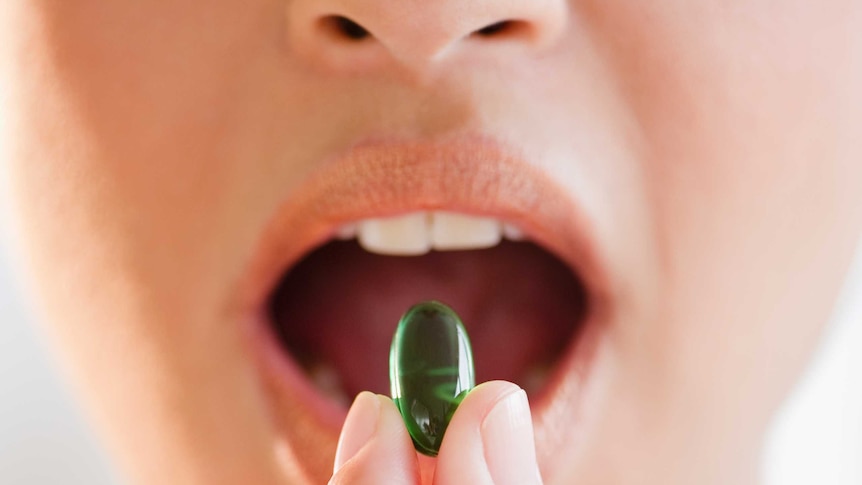 A woman putting a vitamin supplement in her mouth.