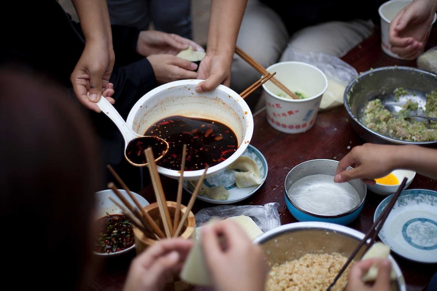 A group of people make Chinese dumplings, with only their arms in the picture, for a story on not eating cultural food.