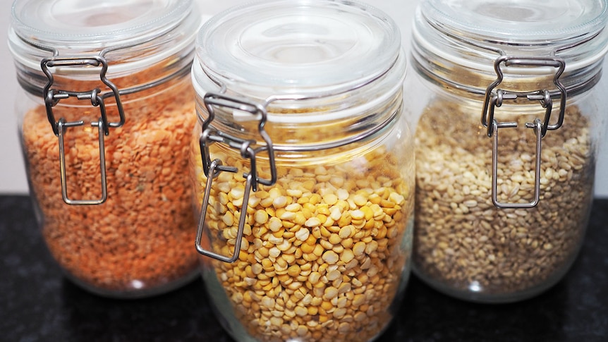 Three glass jars. One filled with red lentils, one with yellow lentils and the third with barley.