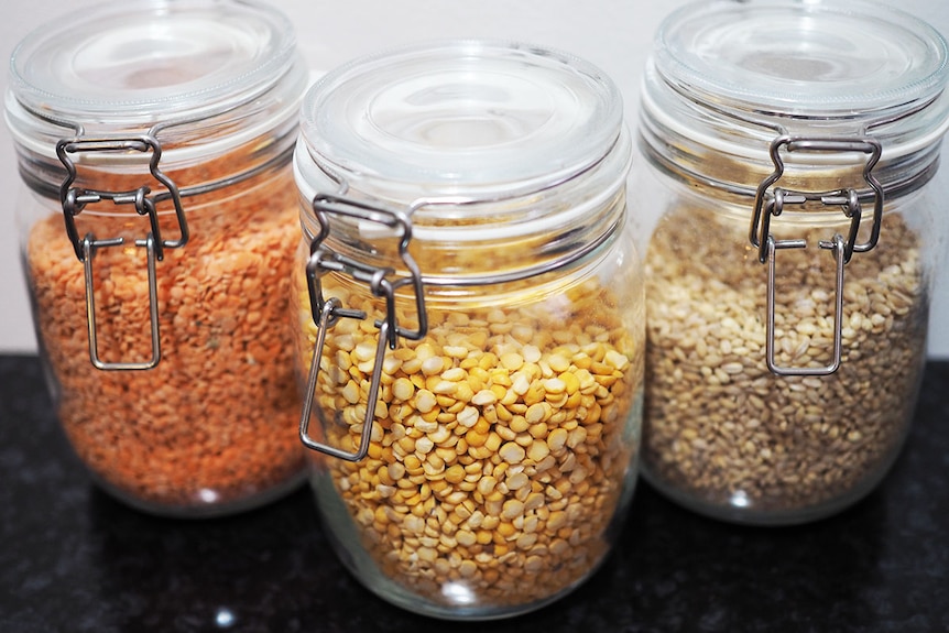 Three glass jars. One filled with red lentils, one with yellow lentils and the third with barley.