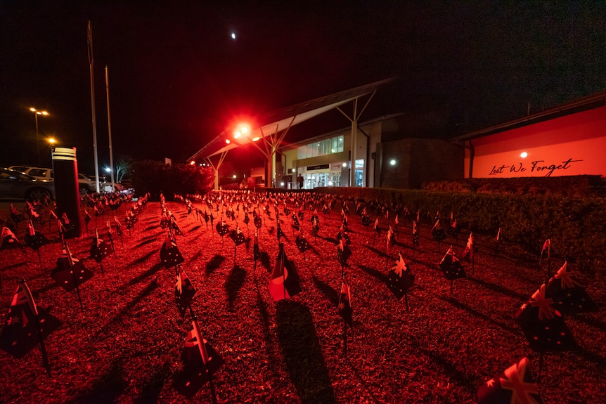 Australian and Aboriginal flags on a lawn at night, bathed in red light.