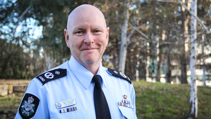 A bald man in police uniform smiles at the camera.