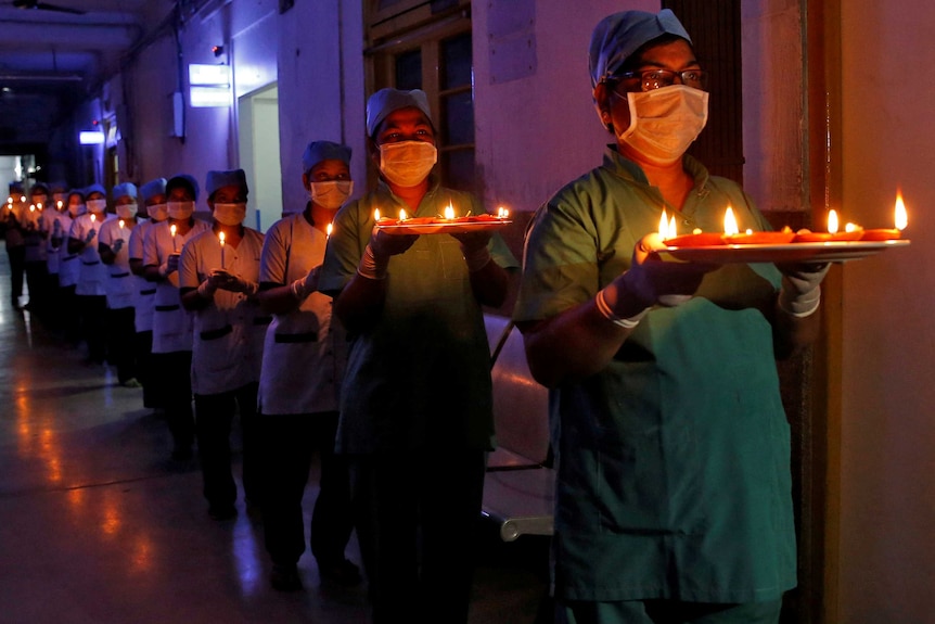 Staff members wearing scrubs and masks carry candles and oil lamps inside a hospital