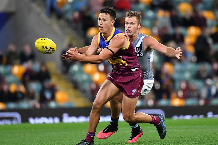 An AFL player handballs the ball as a defender tries to grab him from behind.