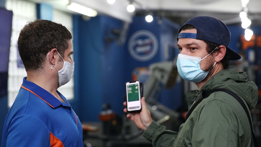 A man presents his vaccination certificate on his phone to a staff member wearing a mask.