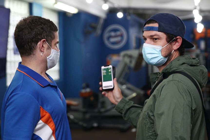 A man presents his vaccination certificate on his phone to a staff member wearing a mask.