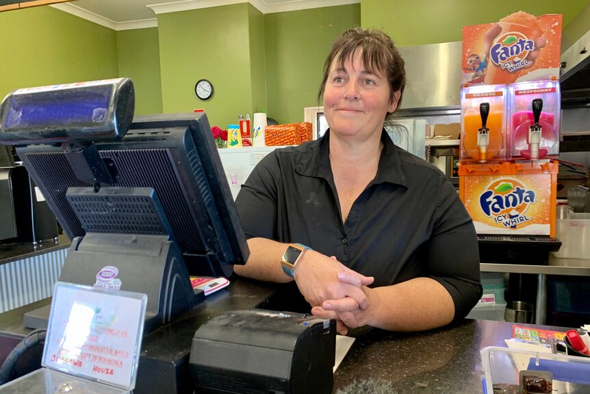 Cafe owner, Judy Mitchell stands behind her counter, at her cash register.
