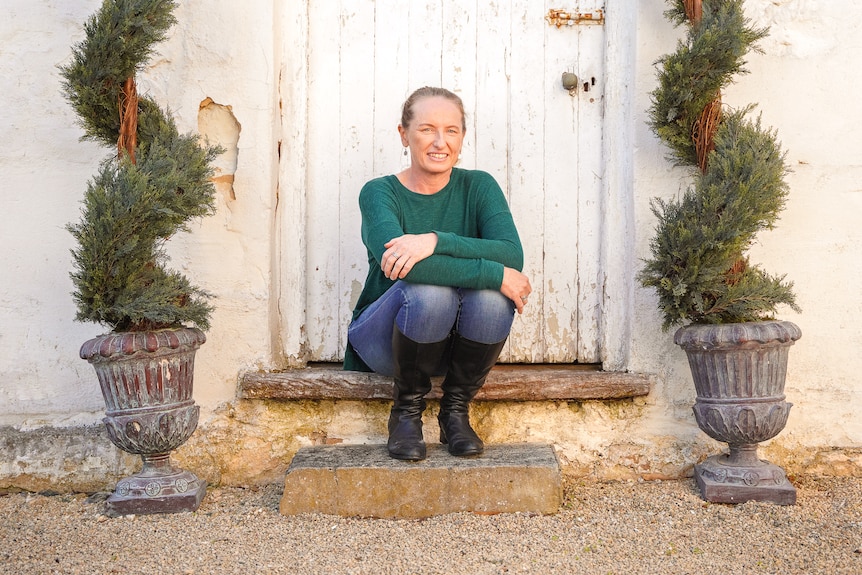 A woman wearing a green top and jeans sits on the steps of an old stone building.