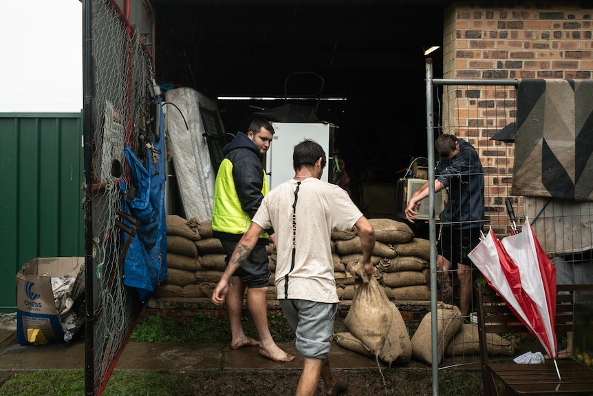 People carry sandbags to place on a wall.