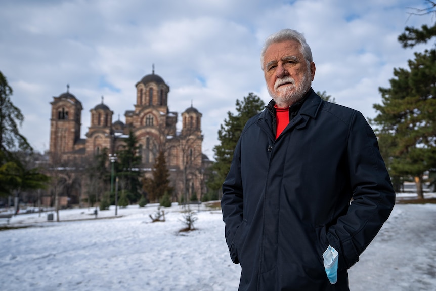 A man with grey hair and a beard poses for a photo in snowy Belgrade.