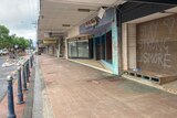 A paved footpath in Lismore with a line of boarded up shops, one with graffiti saying 'stay strong Lismore'
