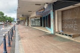 A paved footpath in Lismore with a line of boarded up shops, one with graffiti saying 'stay strong Lismore'