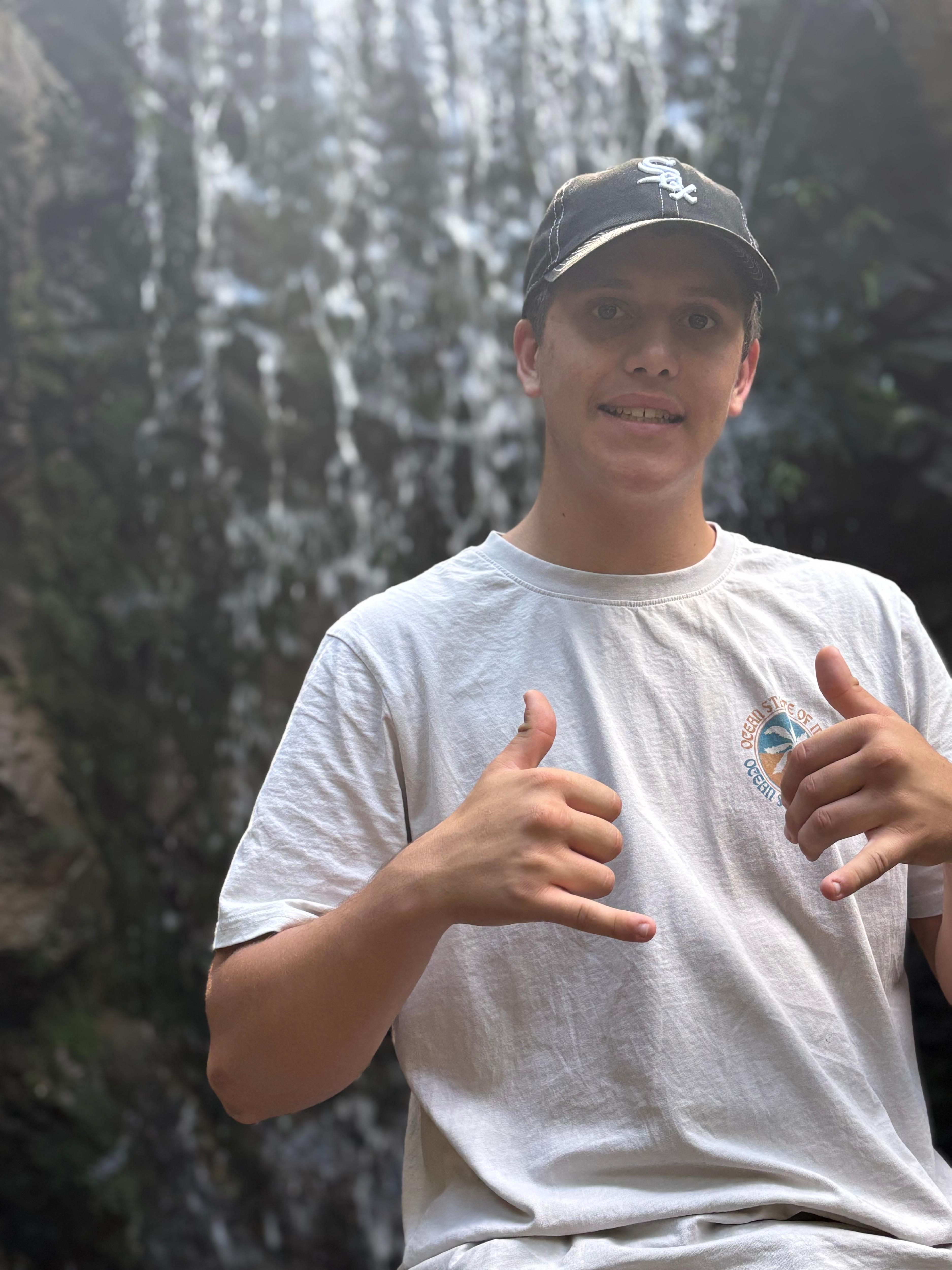 Boy smiles with thumbs up and waterfall behind him