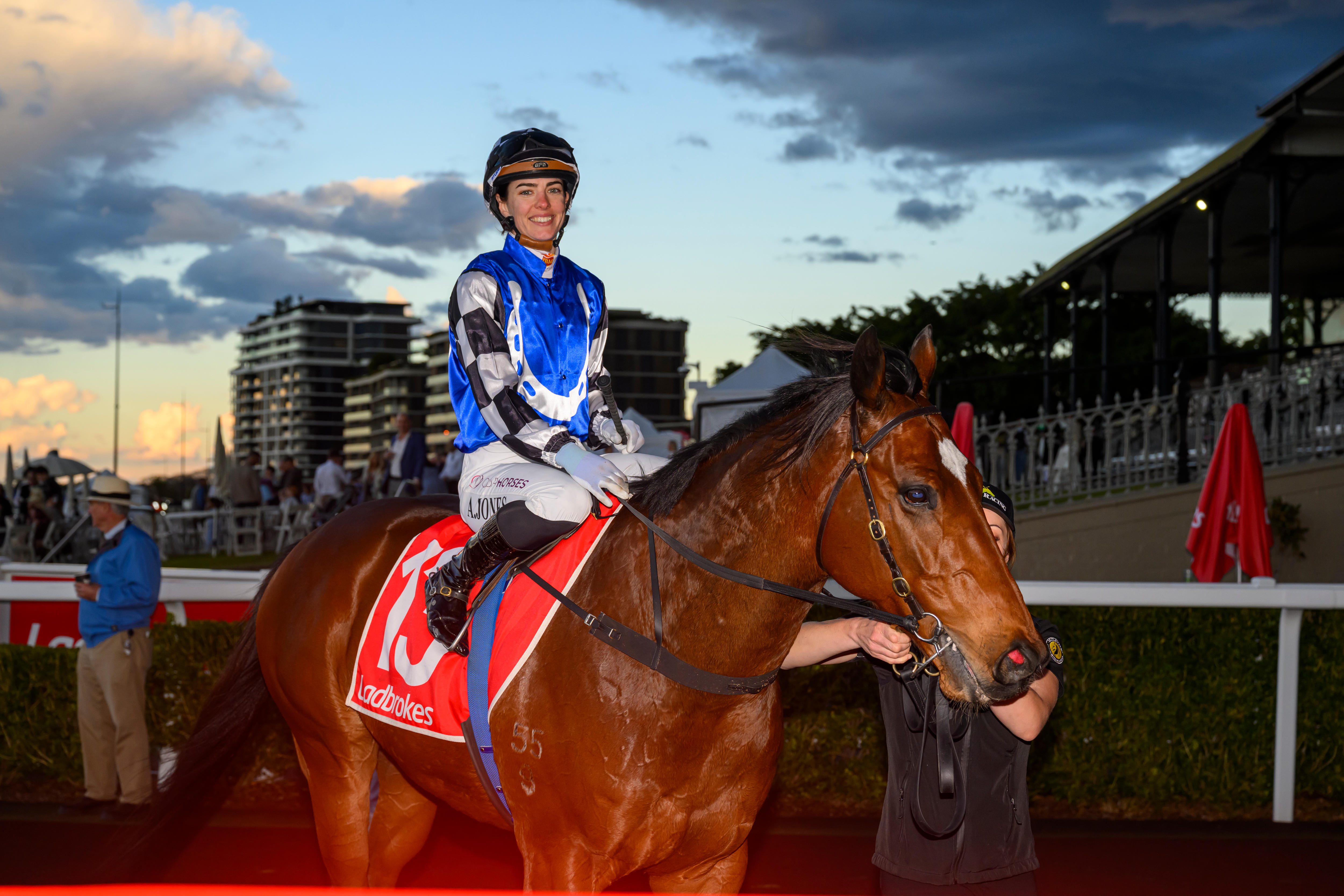 Uma jovem cavaleira vestida com sedas azuis, pretas e brancas está montada em um cavalo.
