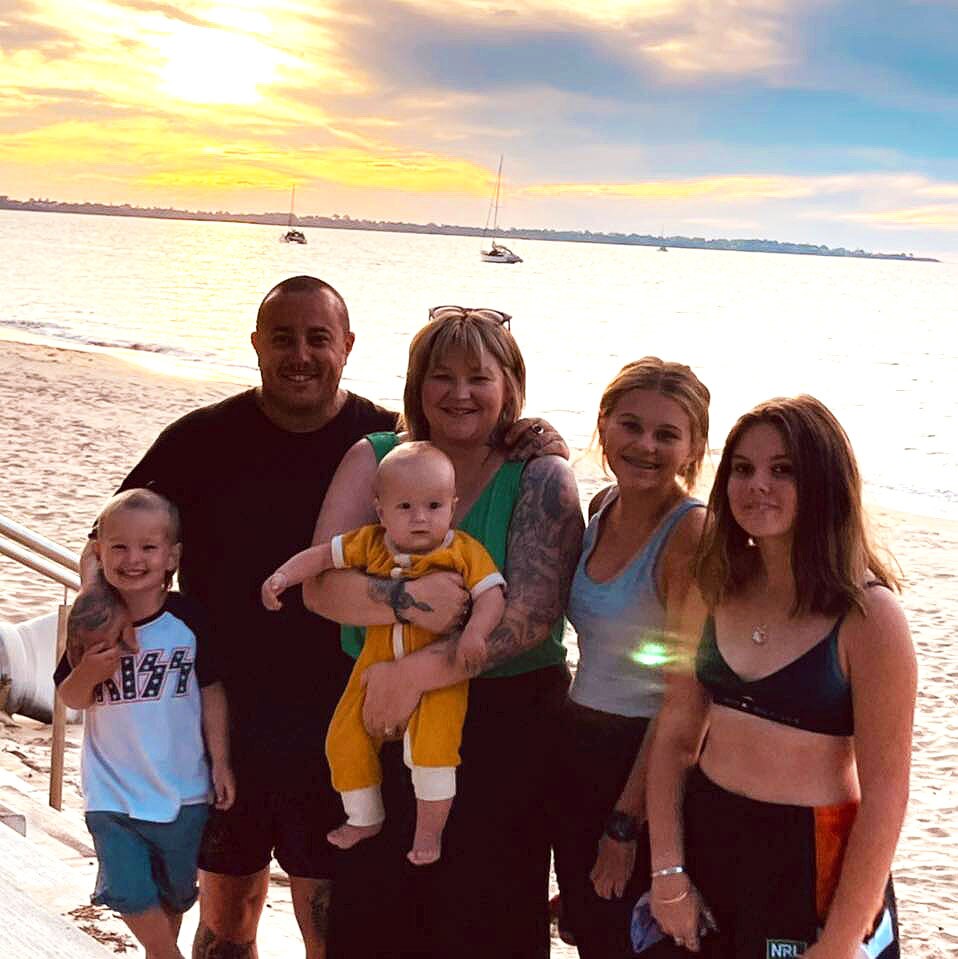 A family of two adults and four kids pose together at the beach.