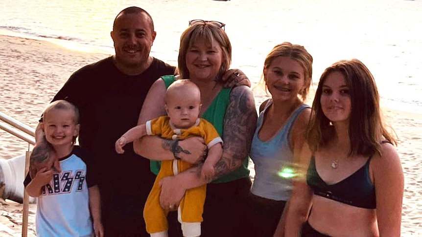 A family of two adults and four kids pose together at the beach.