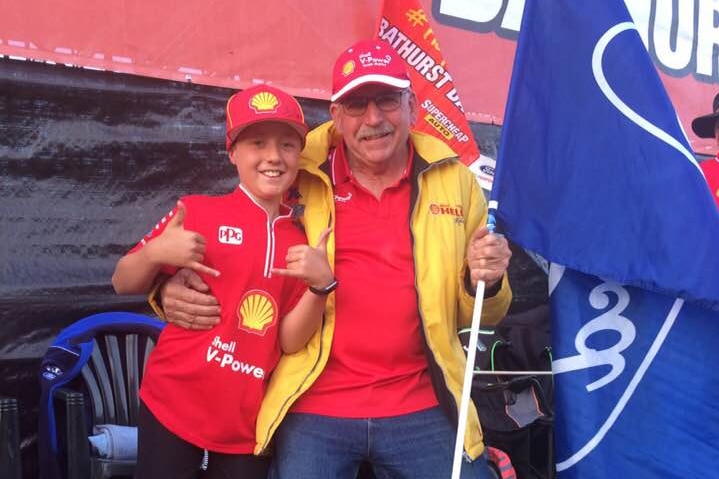 A man and his grandson pose for a photo at a car race.