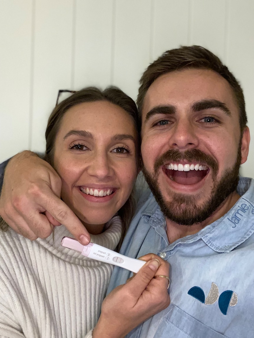 Michelle and Jono taking a selfie, holding a positive pregnancy test.