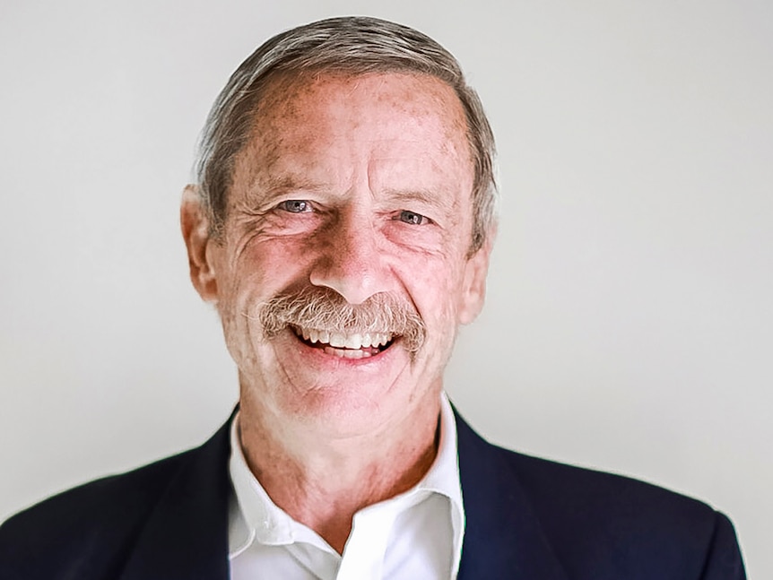 A mustachioed man wearing a dark blazer, smiling widely.