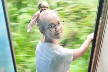 A young girl on a train with a scarf in her hair.