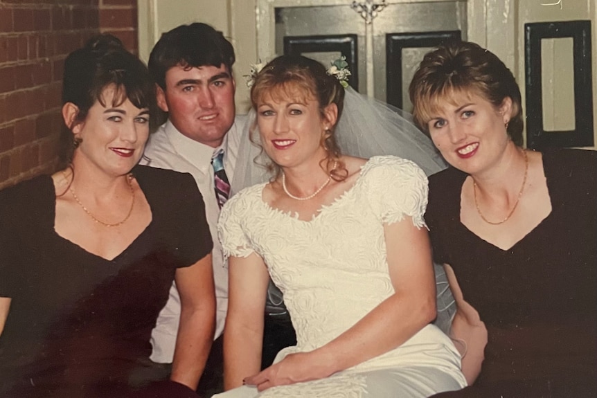 A bride, a man, and two bridesmaids sit in on a step in the front of a house