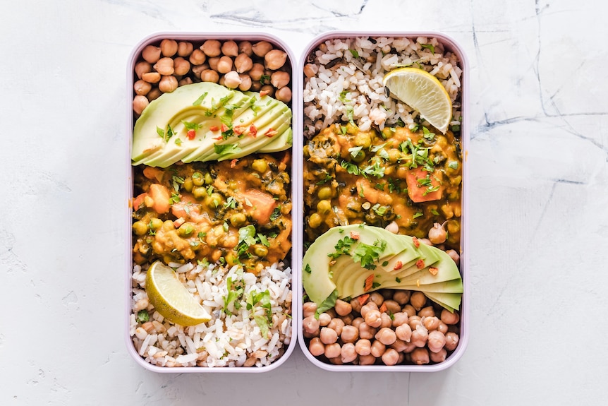 lentils, avocado, curry and rice in a lunchbox with slices of lemon.