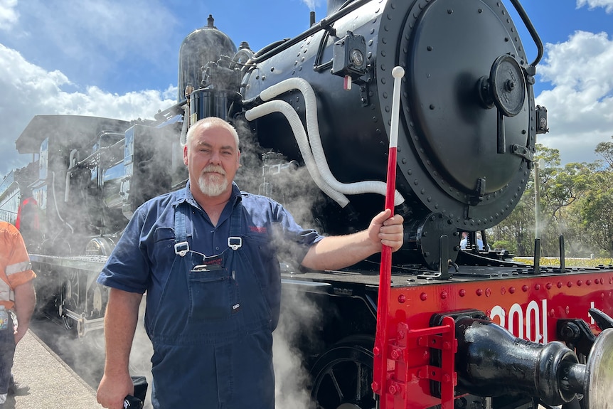 Ben Elliot stands next to the 3001 locomotive wearing blue overalls and holding a part of the train.