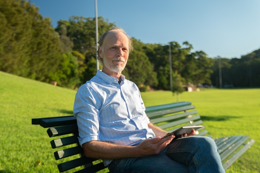 Graham Dawson sits on a park bench with an iPad in his hand