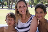 Alira Kelly-Ryder sits in a park with her two sons, with trees and grass in the background.