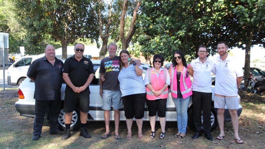 The mechanic, charity workers and members of the cricket club stand with the homeless couple in front of the car