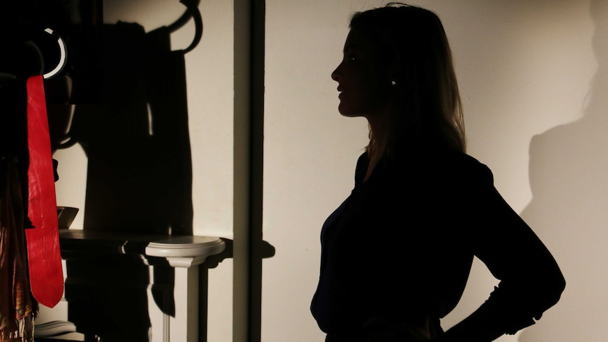 A woman stands silhouetted in shadow inside a bedroom.