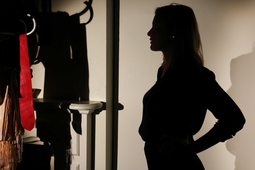 A woman in silhouette stands in front of a rack of clothes.