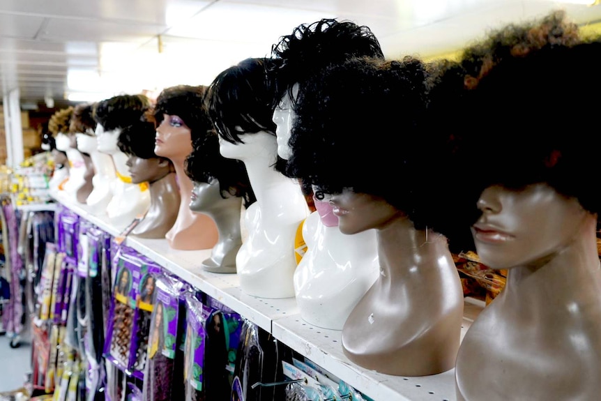 A row of wigs on dummies inside a shop.