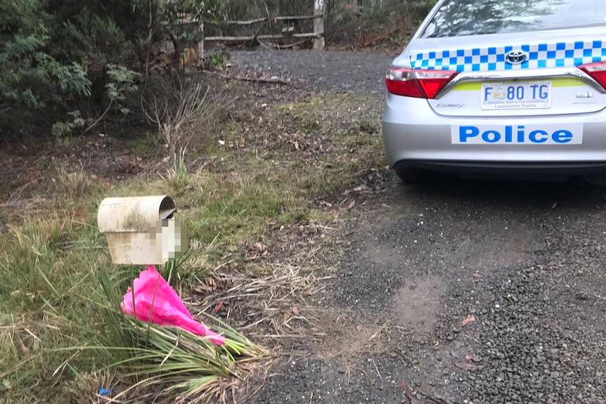 A small bunch of flowers leans against a letter box near a police car.