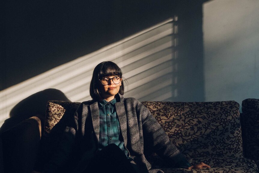 Woman with glasses sitting on a couch and looking to the right for a story about buying a home with your partner.