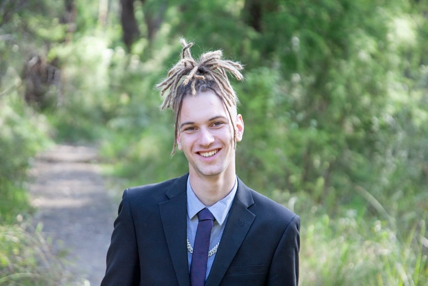 A young man smiles at the camera in an outdoor setting