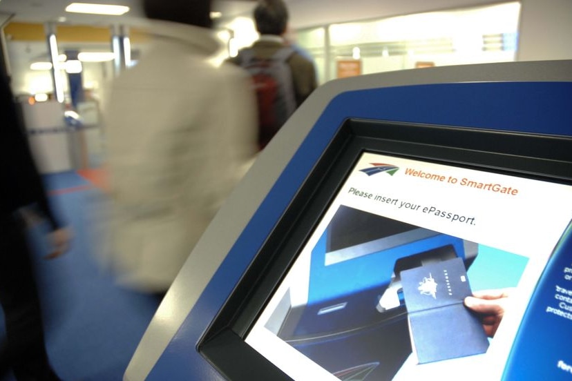 A screen displays the words "Welcome to SmartGate" as passengers walk past it, with their backs to the camera.