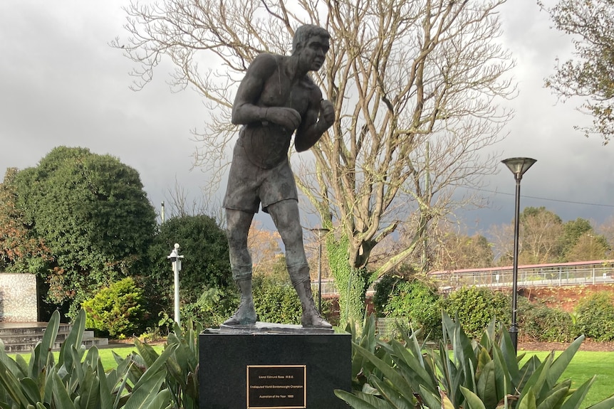 Statue of Lionel Rose sitting in a Warragul park with a two commemorative plaques below it