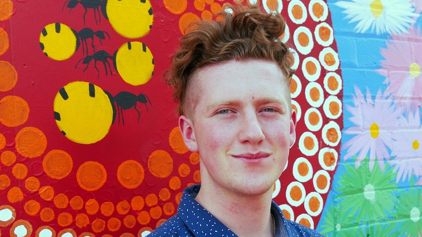 Young man, Blake Hunter, stands in front of colour mural painted on a wall