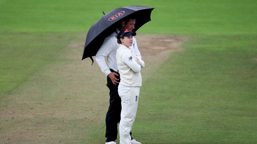 England cricketer Tammy Beaumont stands under an umbrella with an umpire as rain falls during a Women's Ashes Test match.