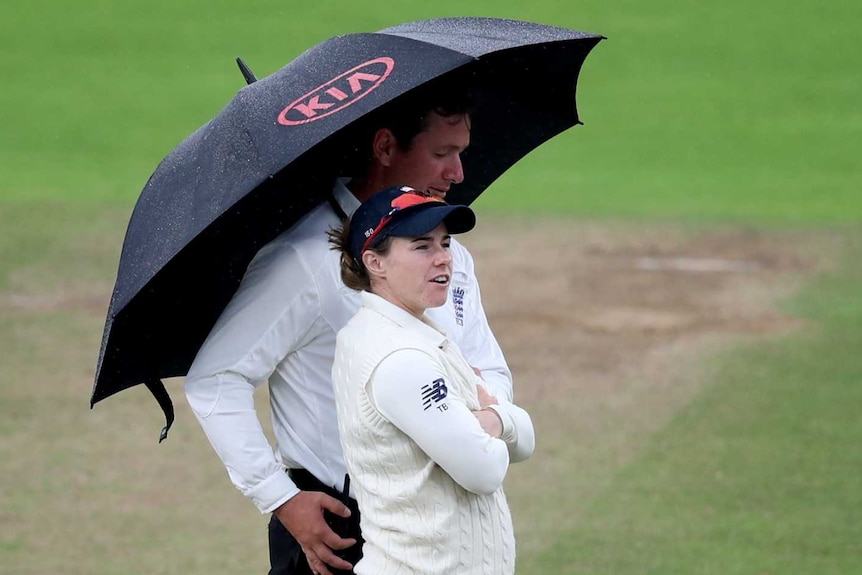 England cricketer Tammy Beaumont stands under an umbrella with an umpire as rain falls during a Women's Ashes Test match.