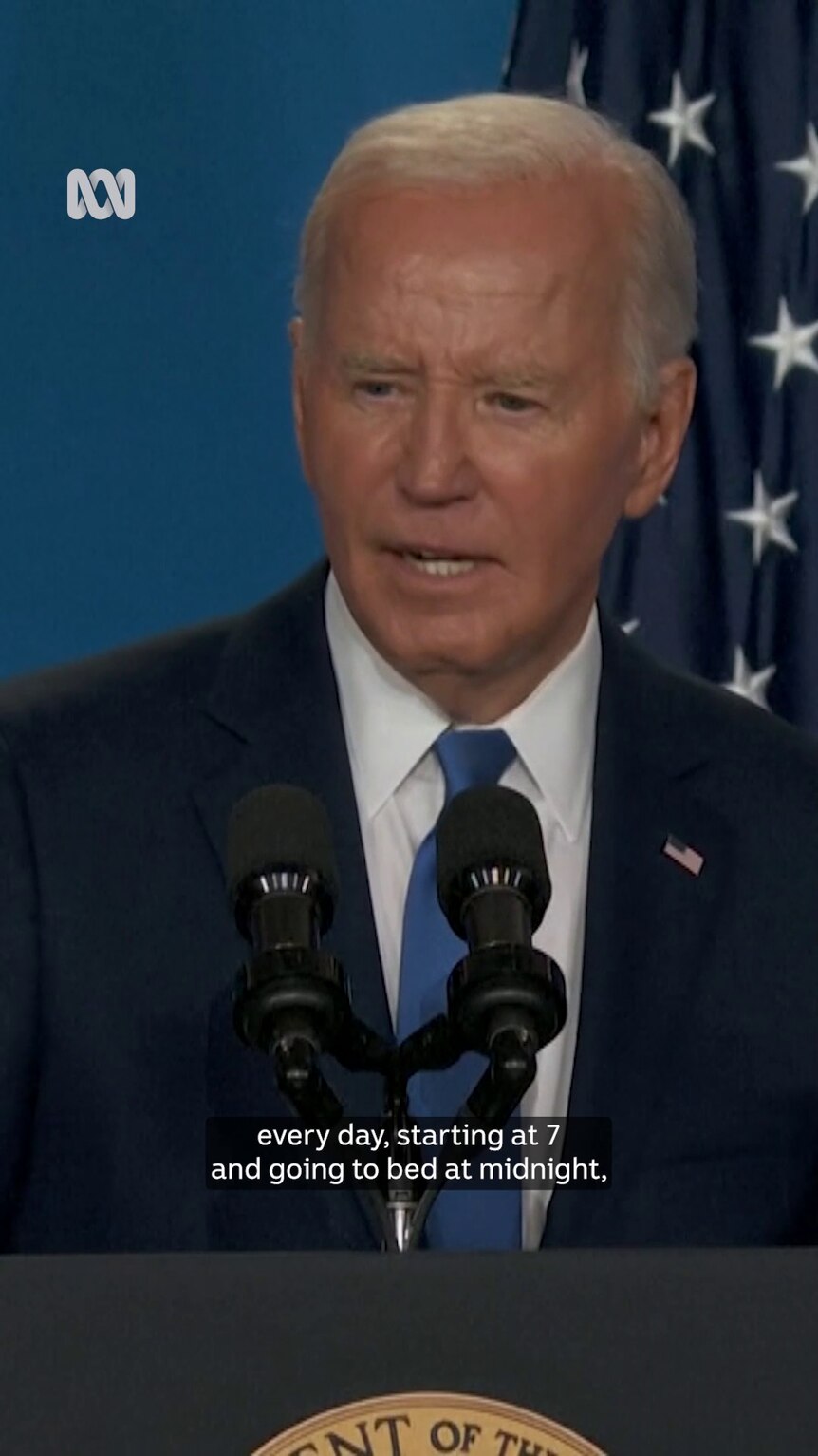 Wearing a suit Joe Biden stands at a lectern with a US flag visible behind him