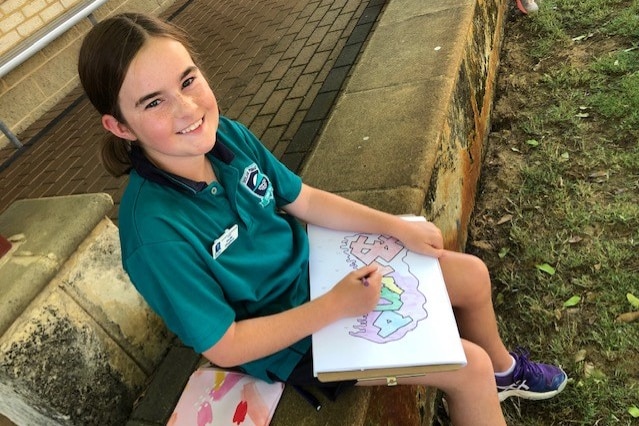 A schoolgirl draws on a large exercise pad while sitting outside