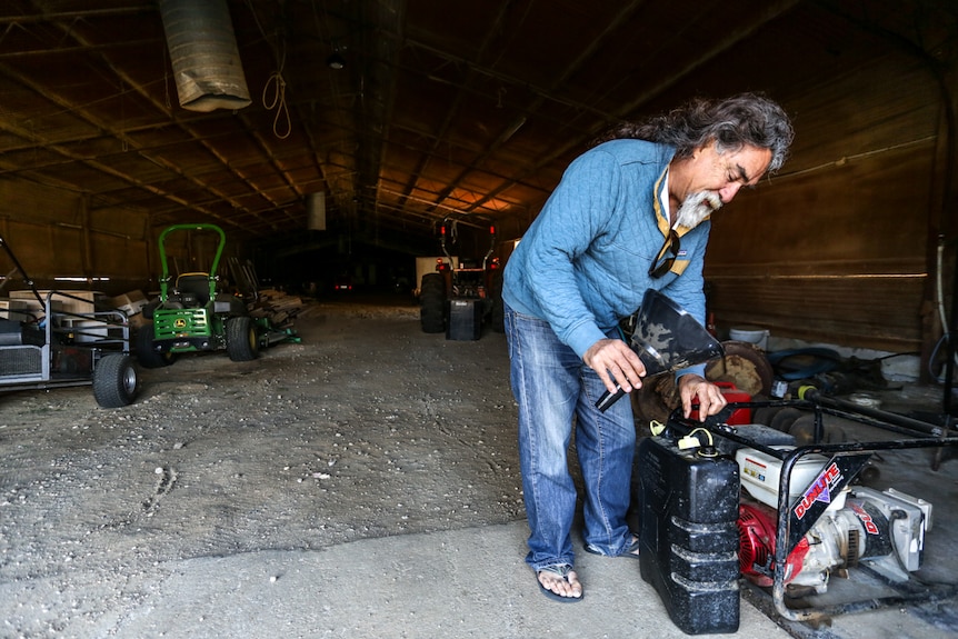 A man leans over a generator in what used to be an old chicken shed on a farmland property in Torquay.