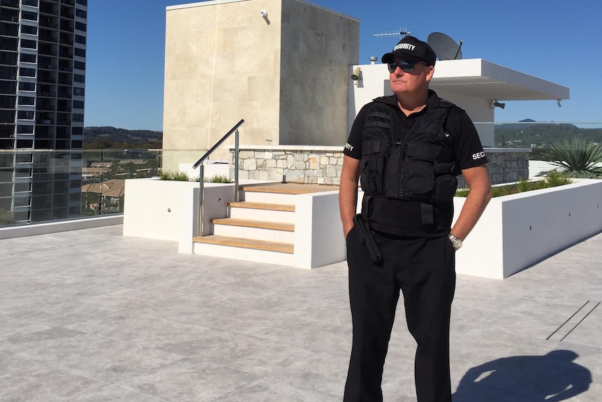 Security guard dressed in black uniform standing on a rooftop.