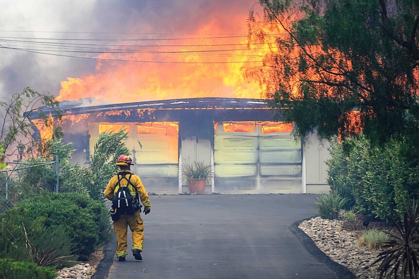 California firefighter approaches a burning home. Fire has torn through the whole property.