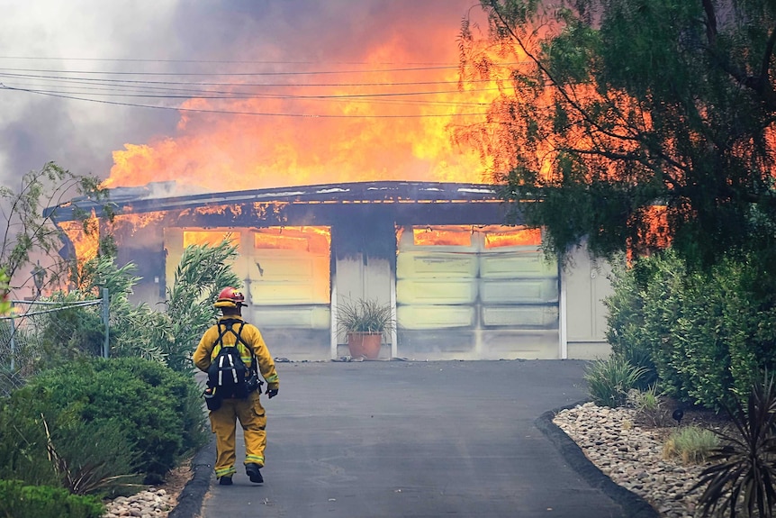 California firefighter approaches a burning home. Fire has torn through the whole property.